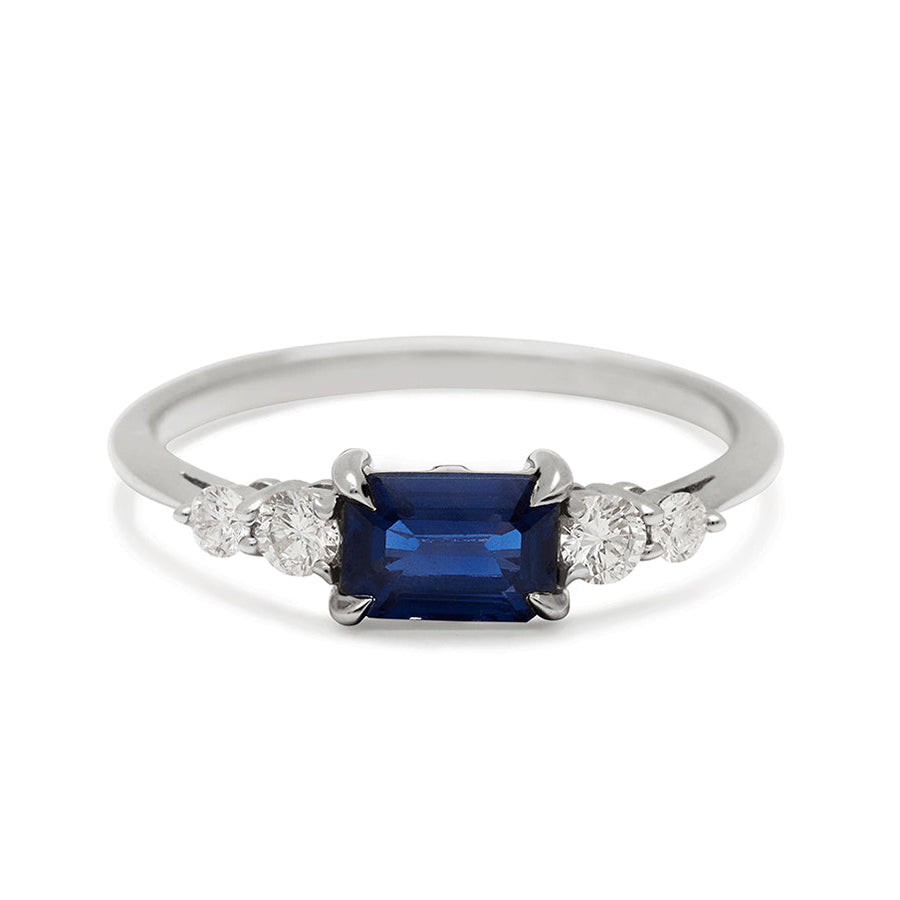 A ring with an emerald cut and shaped blue sapphire center stone with two round white diamonds on either side set in white gold., White Gold