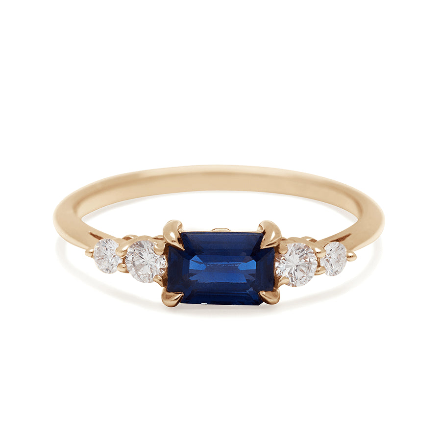 A ring with an emerald cut and shaped blue sapphire center stone with two round white diamonds on either side set in yellow gold., Yellow Gold