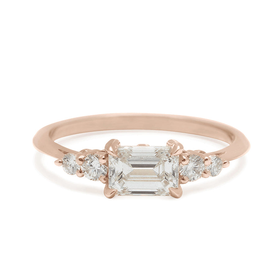 A ring with an emerald cut and shaped white diamond center stone with two round white diamonds on either side set in rose gold., Rose Gold