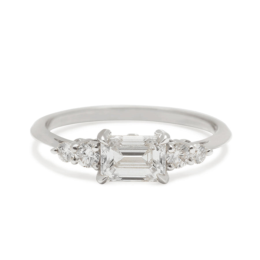 A ring with an emerald cut and shaped white diamond center stone with two round white diamonds on either side set in white gold., White Gold
