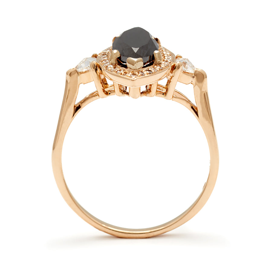 Side view of a three stone engagement ring with an marquise shape black diamond center stone surrounded by a white diamond pave halo with two white diamond trillion side stones set in yellow gold.