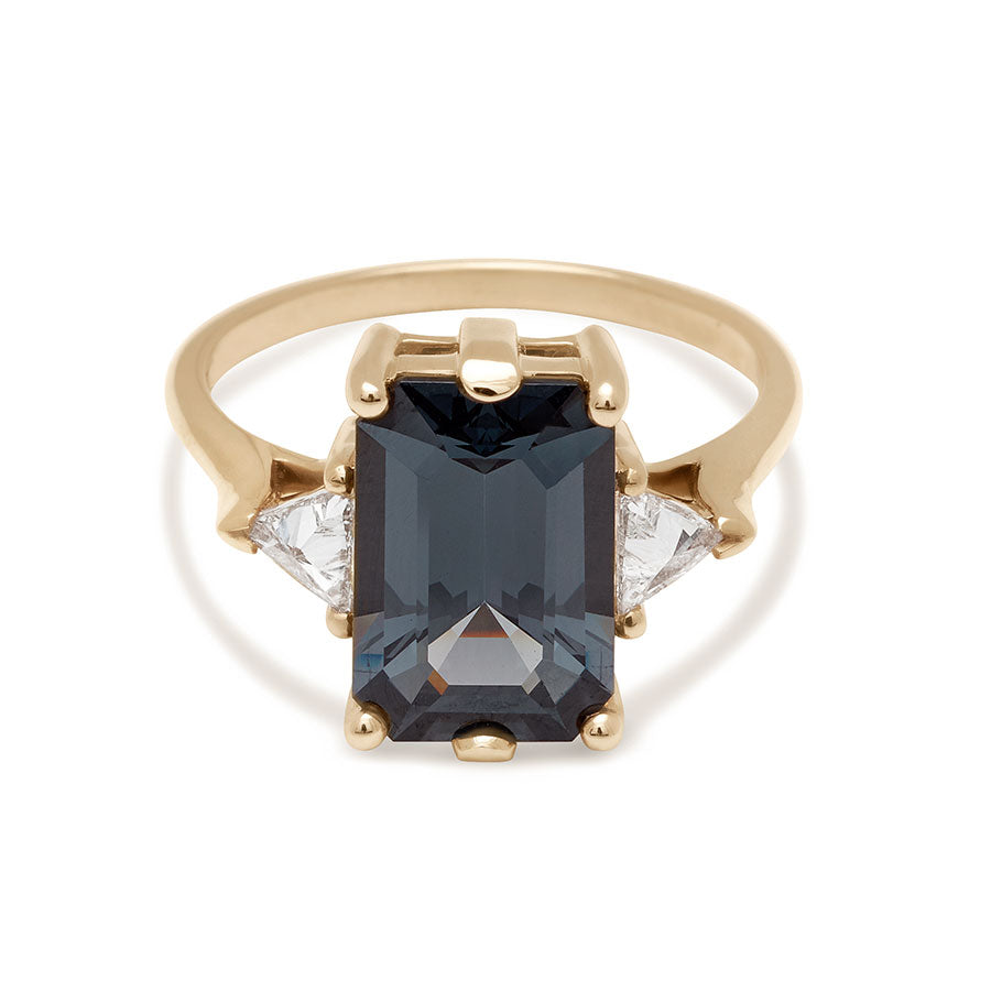 A three stone engagement ring with an emerald shape grey spinel center stone with two white diamond trillion side stones set in yellow gold.