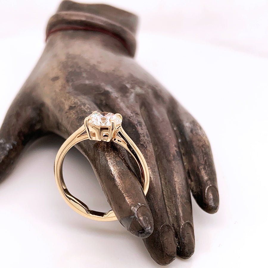 A solitaire round white diamond ring with claw prongs set in yellow gold being held by a stone hand.