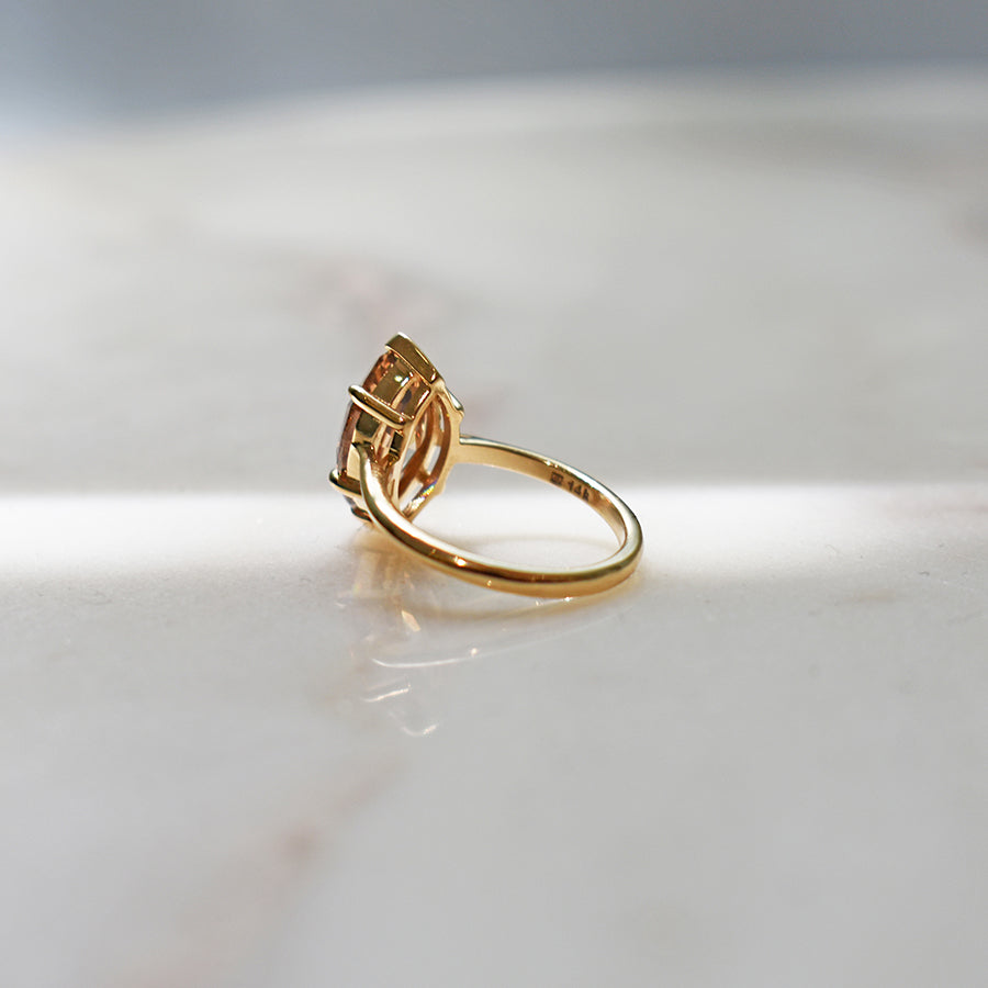 An solitaire ring with a marquise shape champagne diamond stone set in a yellow gold band on a grey background.