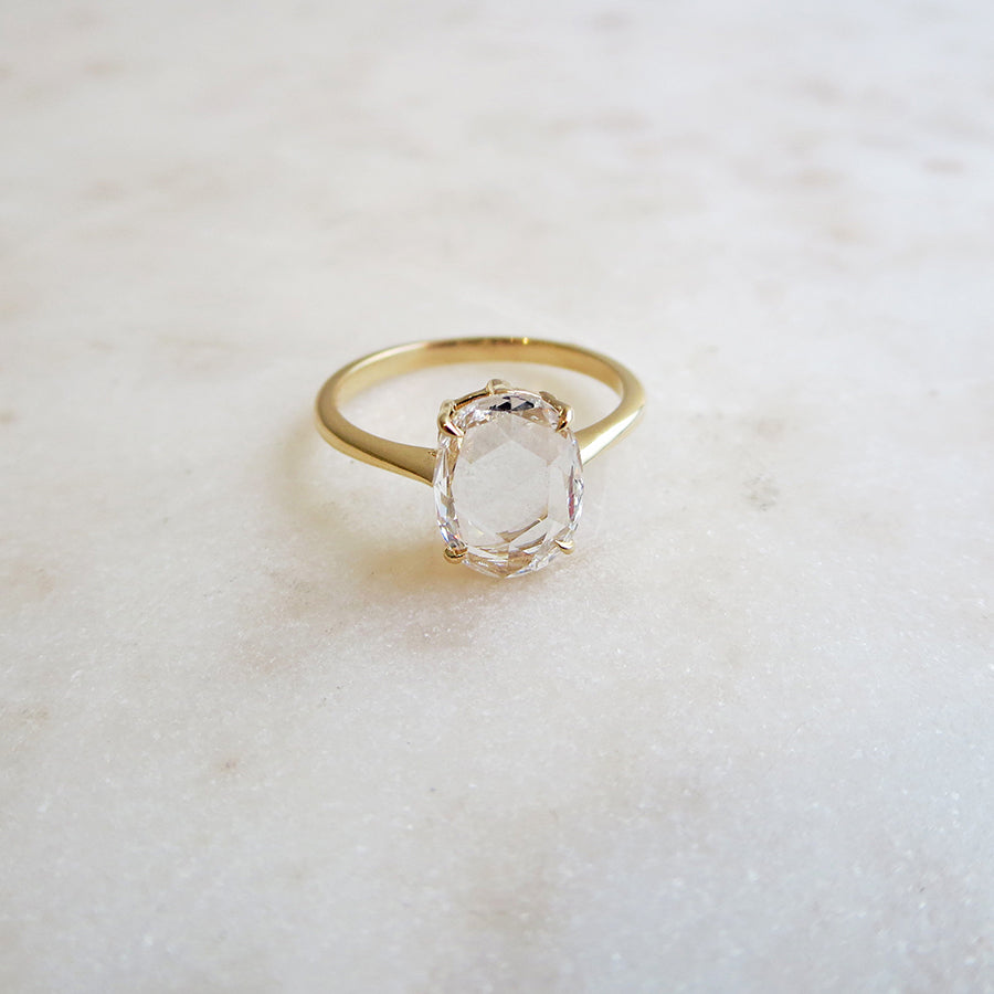 A solitaire ring rose cut oval white diamond set in yellow gold on a grey background.