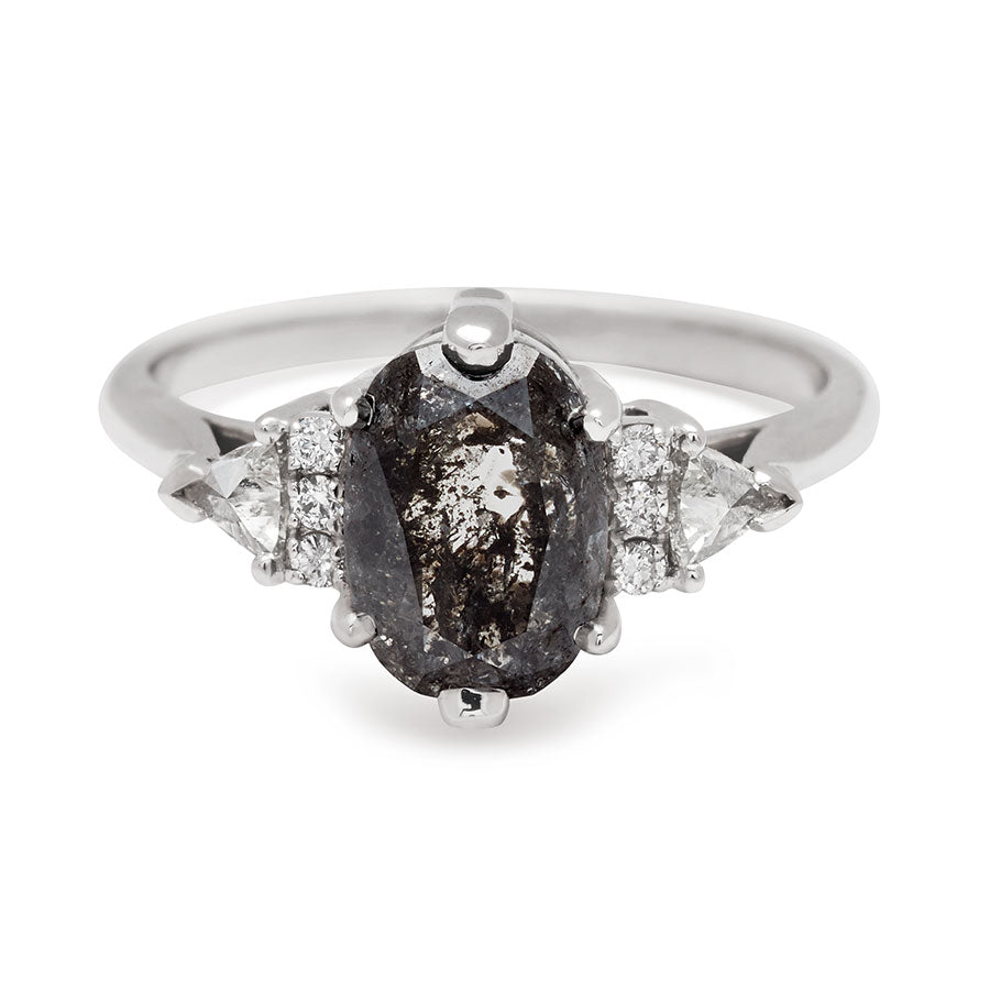 An oval shape grey diamond center stone ring with three round white diamonds on either and two white diamond trillions on the outer edges of each side set in white gold.