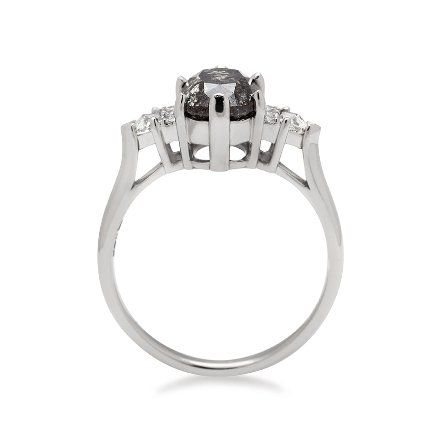 Side view of an oval shape grey diamond center stone ring with three round white diamonds on either and two white diamond trillions on the outer edges of each side set in white gold.