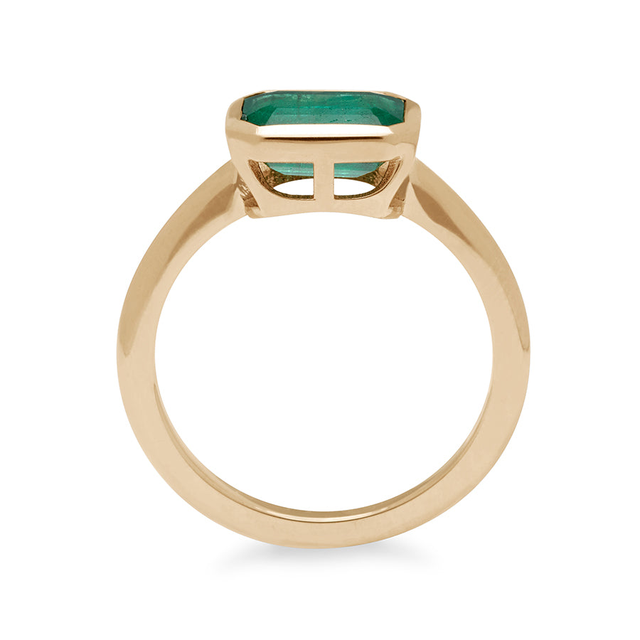 Side view of an east/west emerald shape bezel set green emerald center set in yellow gold.
