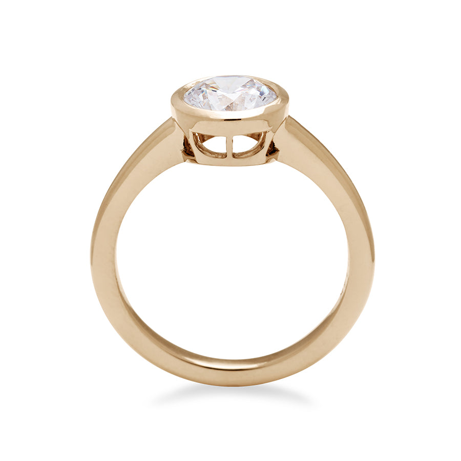 Side view of a round brilliant cut bezel set white diamond set in yellow gold.