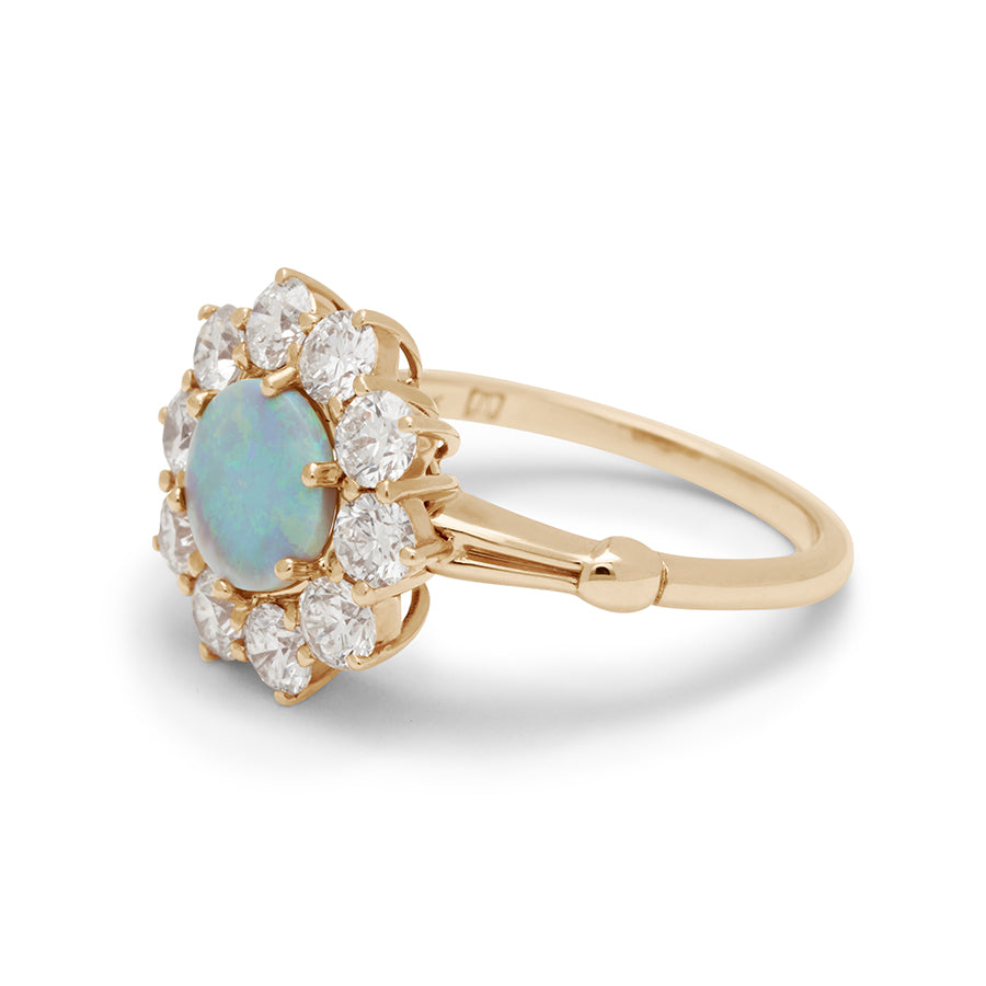 Angled view of a ring with a round opal center stone surrounded by round white diamonds set in a yellow gold band.