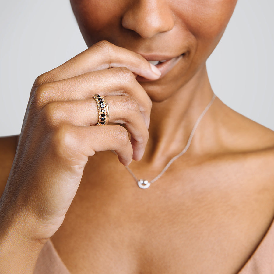 A band with round black diamonds in a 3/4 pave around a rose gold band with white diamond accents on both top and bottom on a medium-complexion model with a solid yellow gold band.