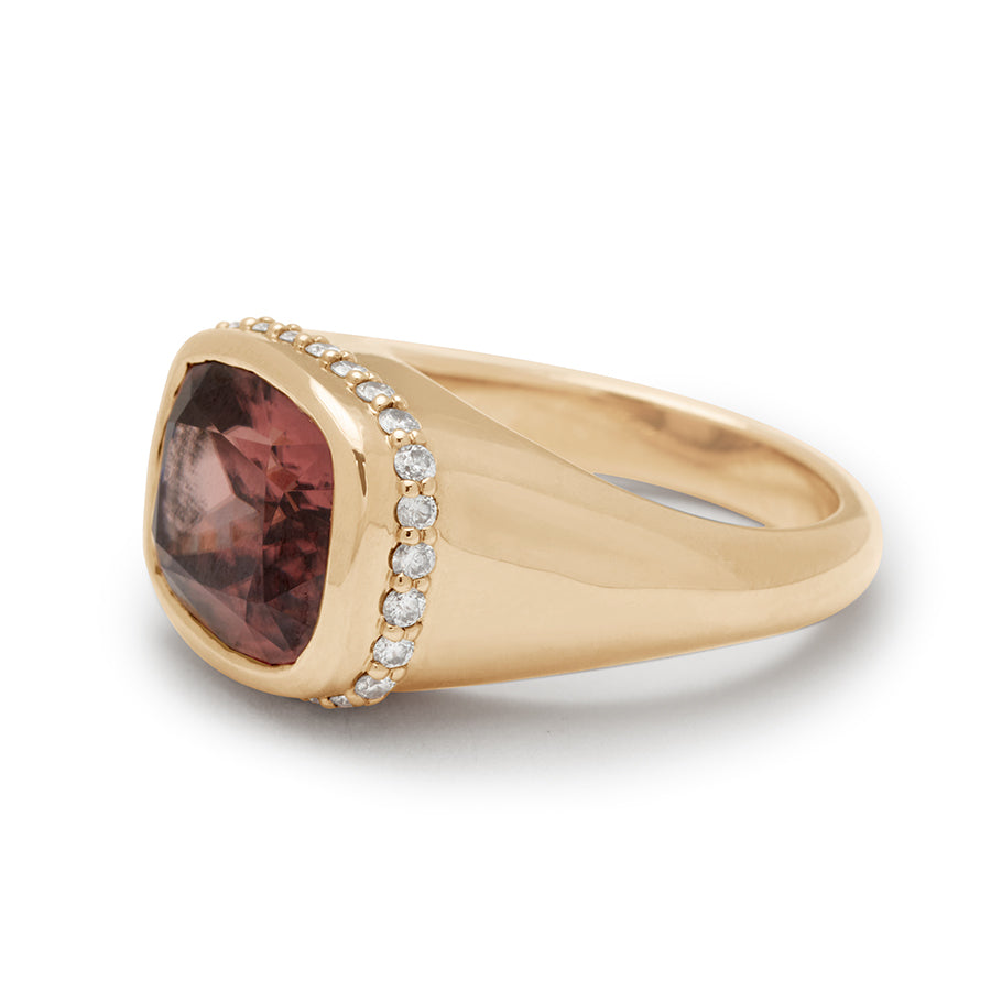 Angled view of a cushion cut zircon stone set in a signet style with a white diamond pave halo set in yellow gold.