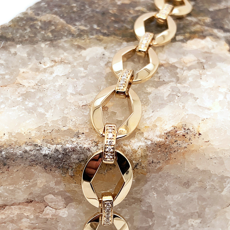 Zoomed in view of a large chain bracelet with white diamond accents set in yellow gold on a stone.
