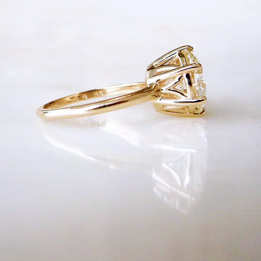 Angled view of a solitaire ring round white diamond set in yellow gold.