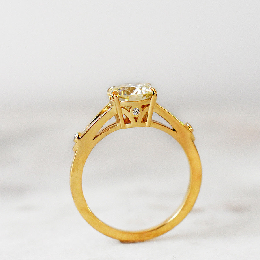 Side view of a ring with a round white diamond with double claw prong with triangle accent gold on either side set in yellow gold on a grey background.