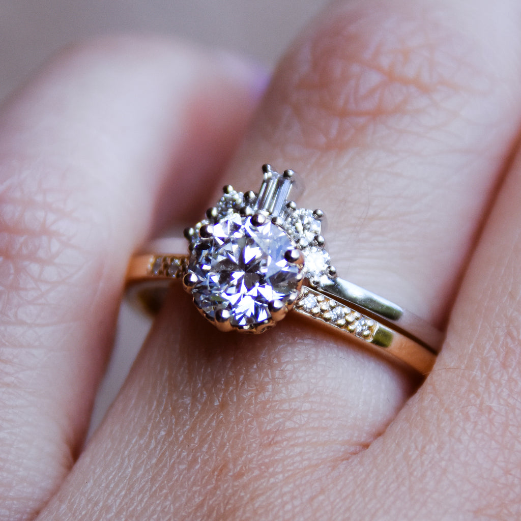 A white diamond baguette band with two round diamonds on either side set in yellow gold above a solitaire white diamond ring set in yellow gold on a light-complexion hand, made in Yellow Gold, Rose Gold, or White Gold.
