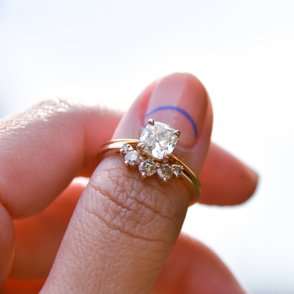 A curved 5 white diamond band set in yellow gold below a knife edge ring with a white diamond center stone on a light-complexion hand.
