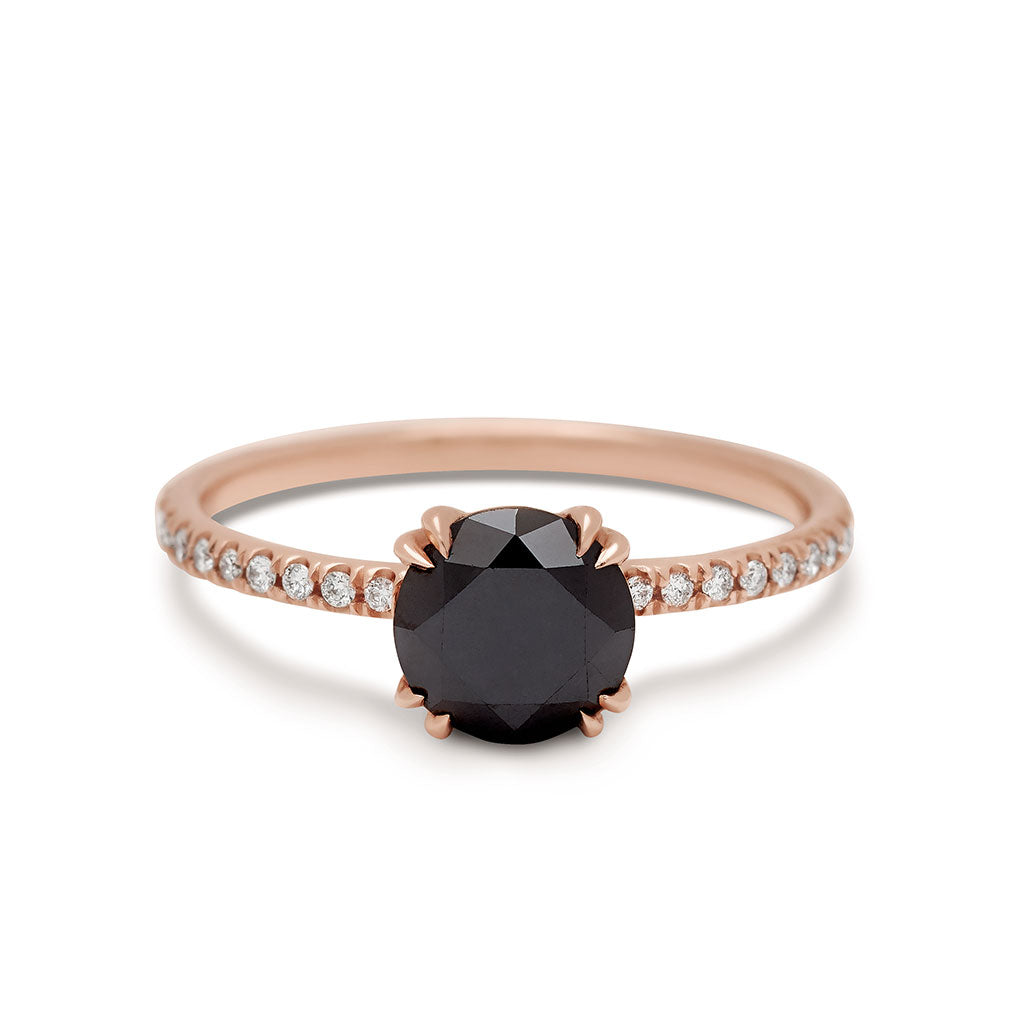 A solitaire round black diamond ring with double claw prongs with white diamond pave on the band set in rose gold.