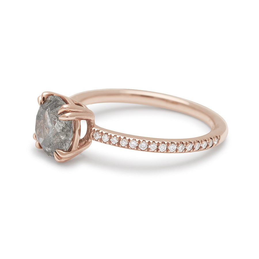 Angled view of a solitaire round grey diamond ring with double claw prongs with white diamond pave on the band set in rose gold.