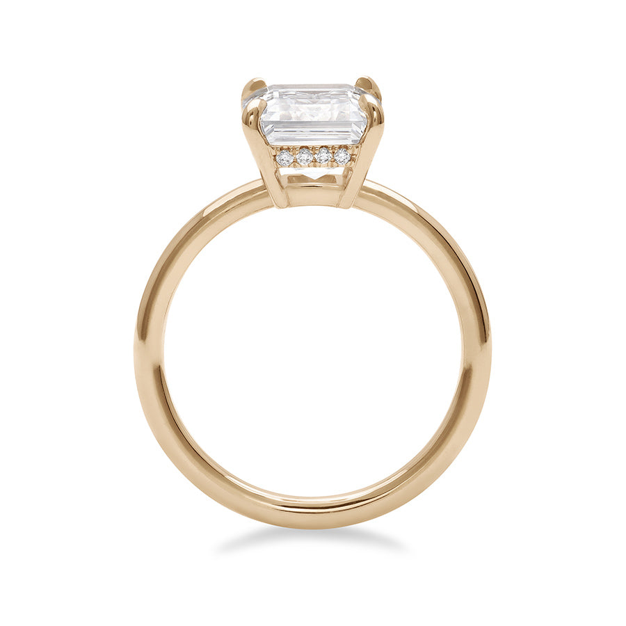 Side view of an emerald cut and shaped white diamond solitaire engagement ring with a hidden white diamond pave halo under the center stone set in yellow gold.