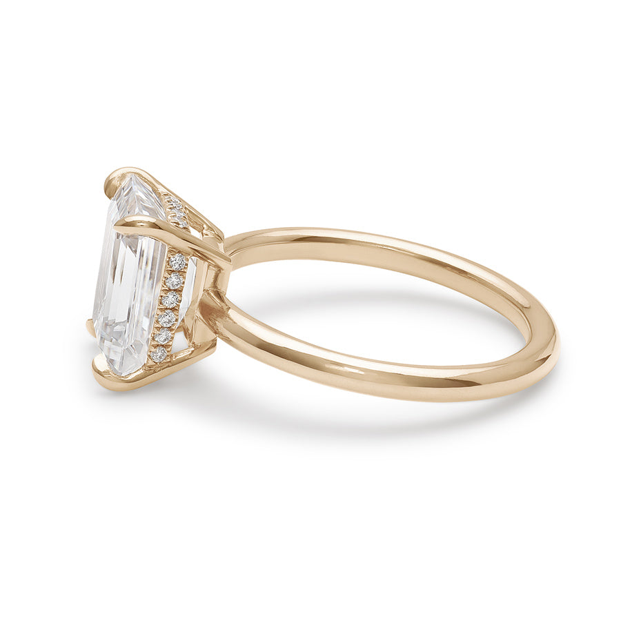 Angled view of an emerald cut and shaped white diamond solitaire engagement ring with a hidden white diamond pave halo under the center stone set in yellow gold.