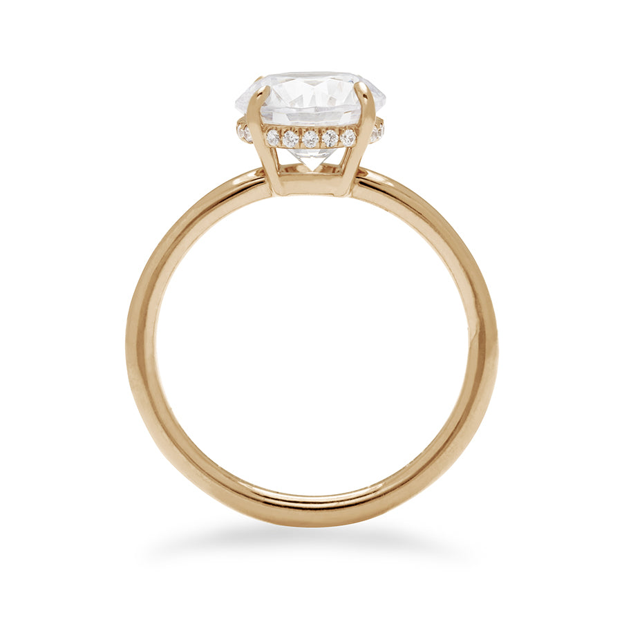 Side view of a round shaped white diamond solitaire engagement ring with a hidden white diamond pave halo under the center stone set in yellow gold.