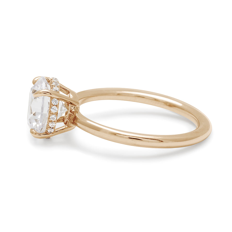 Angled view of a round shaped white diamond solitaire engagement ring with a hidden white diamond pave halo under the center stone set in yellow gold.