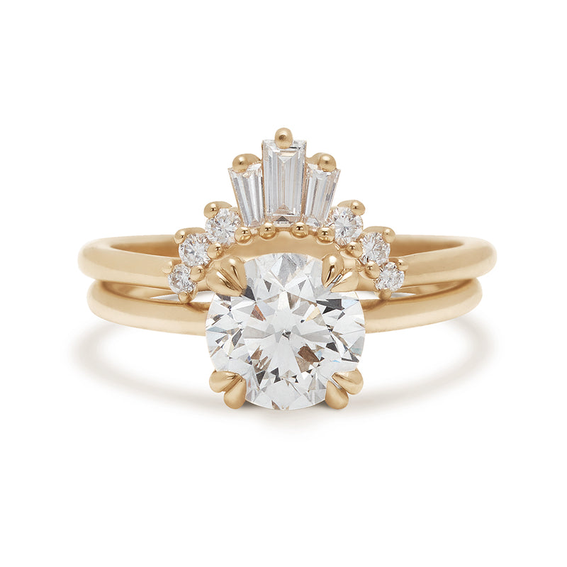 A solitaire round white diamond ring with double claw prongs set in yellow gold above a triple baguette white diamond band in yellow gold.