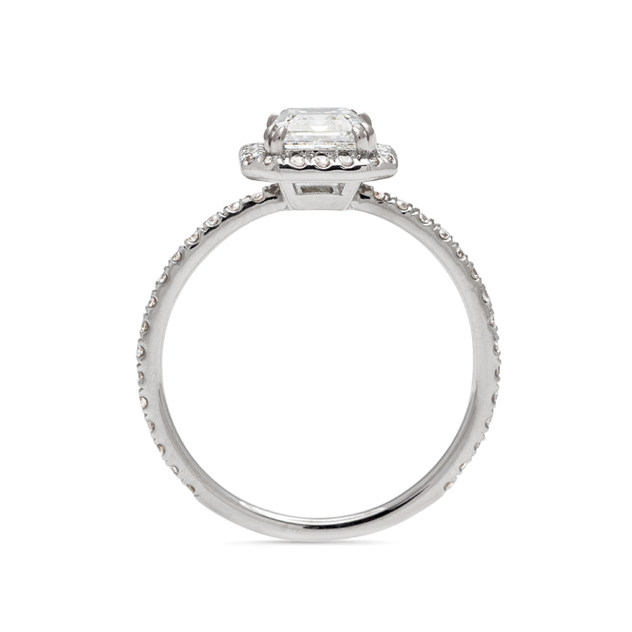 Side view of an engagement ring with an emerald cut white diamond center stone surrounded by a white diamond pave halo set in white gold.