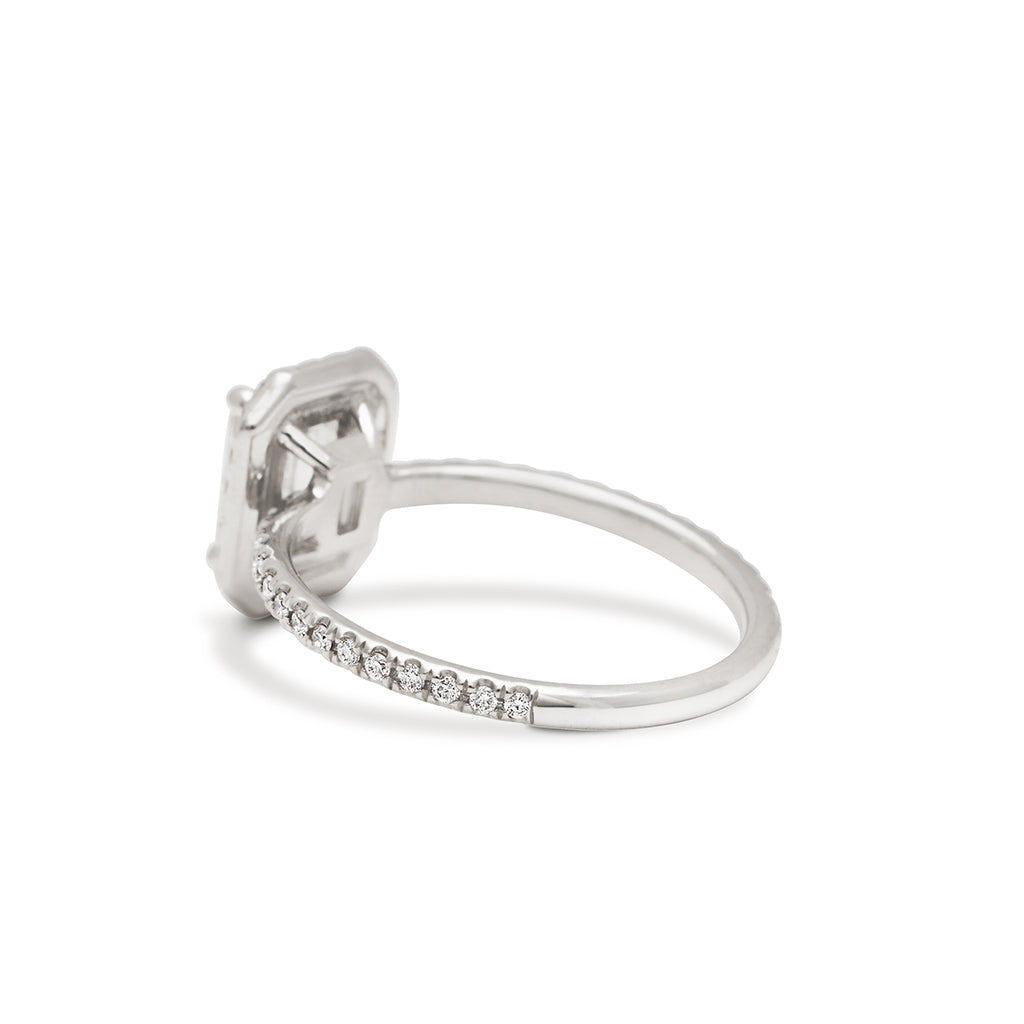 Angled view of an engagement ring with an emerald cut white diamond center stone surrounded by a white diamond pave halo set in white gold.
