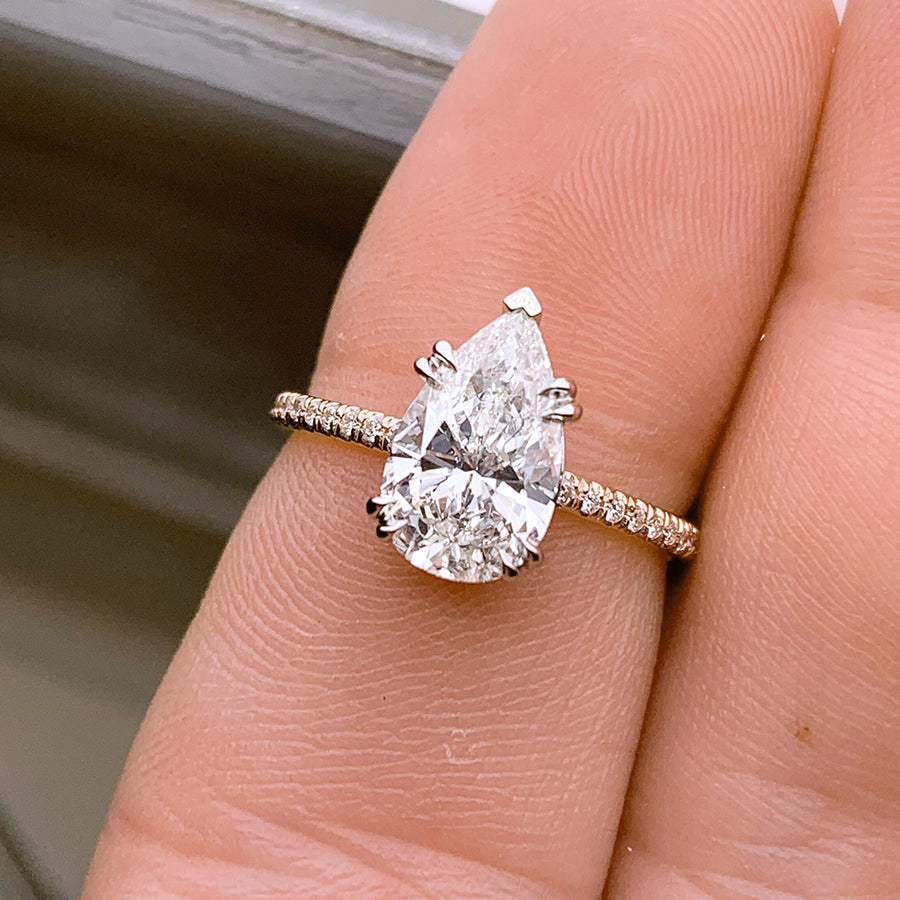 A solitaire pear white diamond ring with double claw prongs with white diamond pave on the band set in white gold medium-complexion finger.