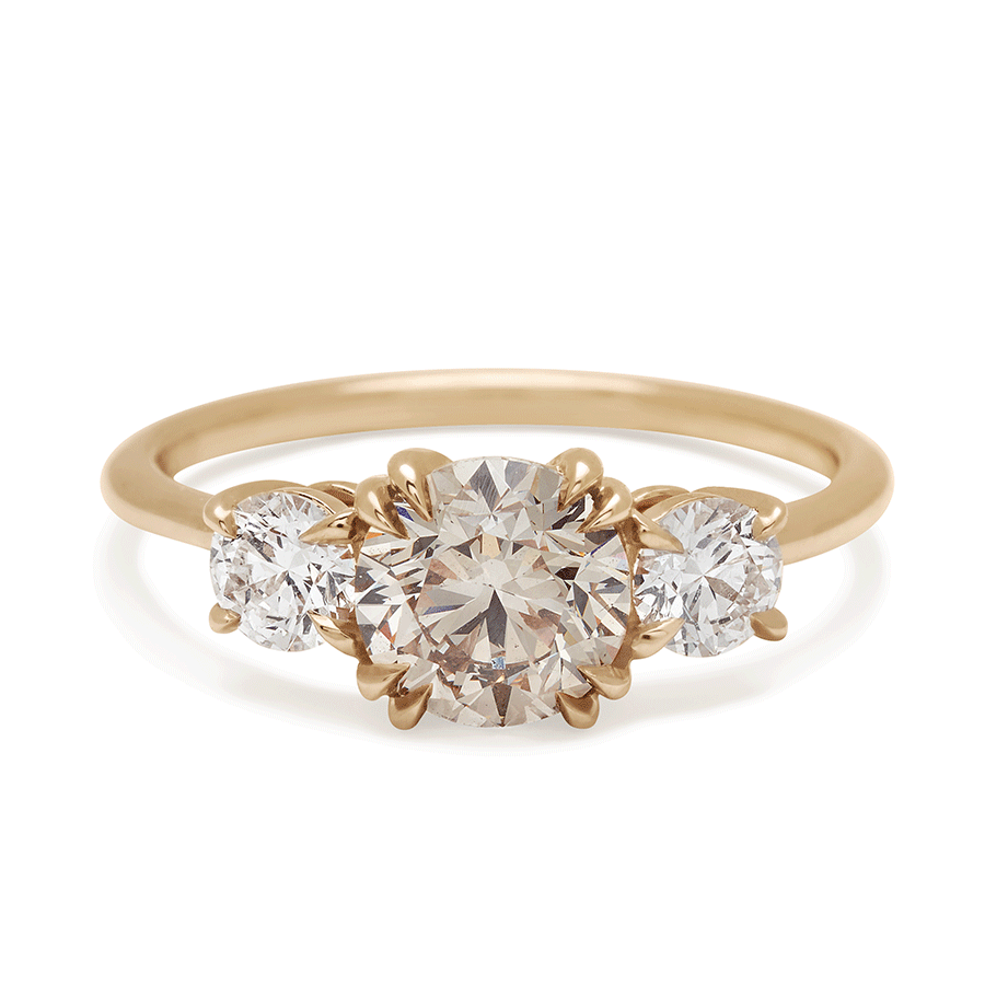 A three stone engagement ring with a round shape champagne diamond center stone with two white diamond round side stones set in yellow gold., Yellow Gold