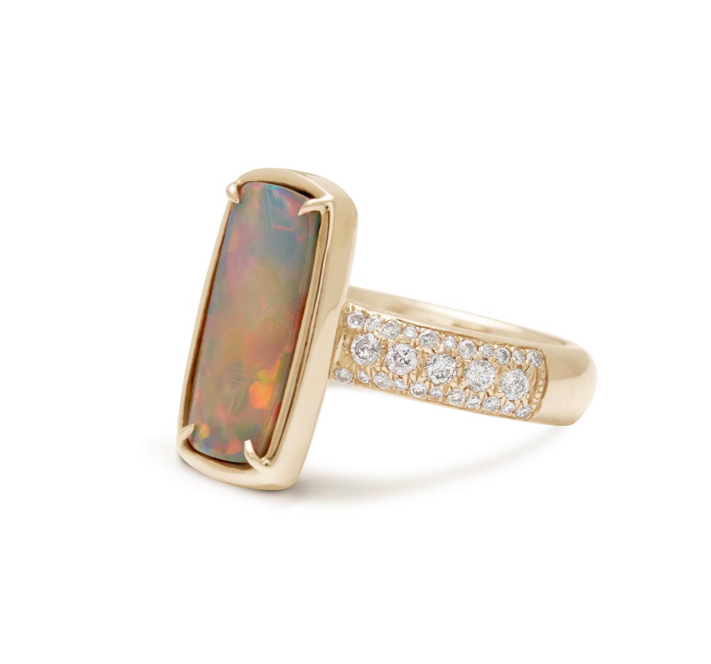 Angled view of a ring with an emerald shaped black opal set in claw prongs and bezel set yellow gold with a white diamond 3/4 pave band.