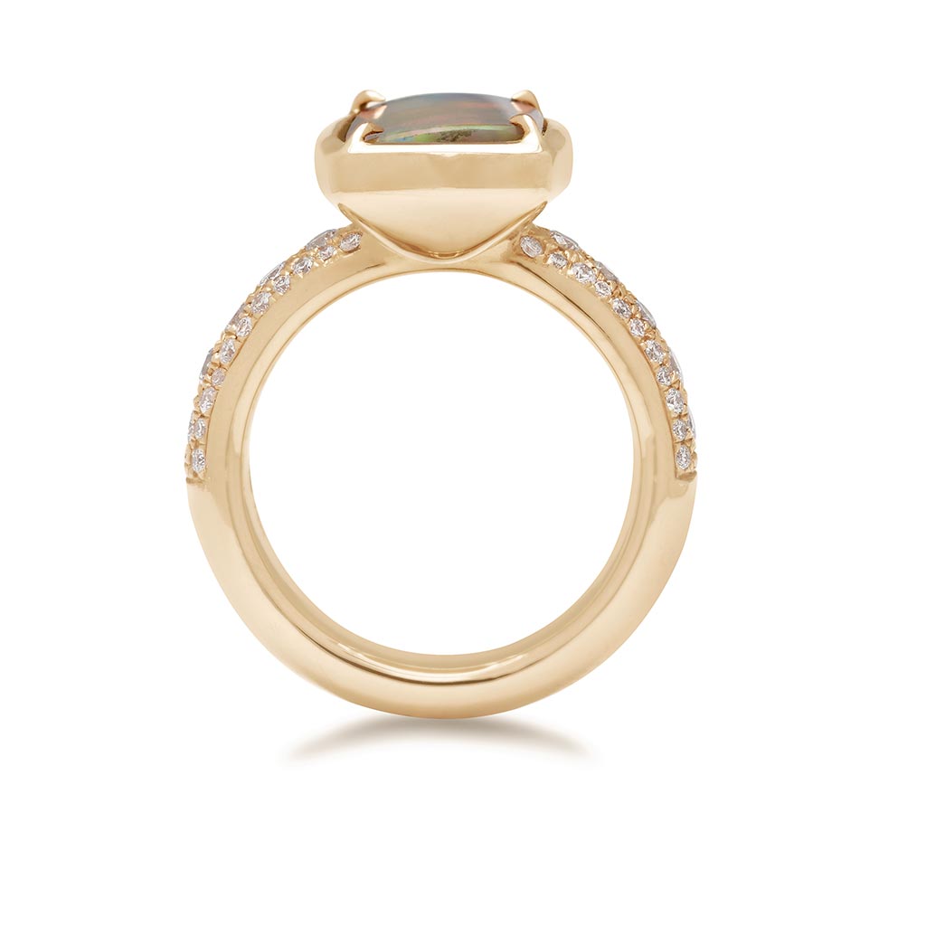 Side view of a ring with an emerald shaped black opal set in claw prongs and bezel set yellow gold with a white diamond 3/4 pave band.