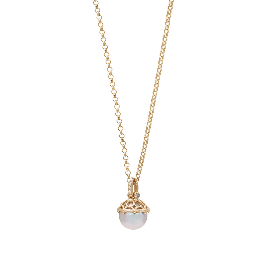 Zoomed out view of a one of a kind light pearl pendant with white diamond pave on the top and grey diamond accent stones on either side on a yellow gold chain.
