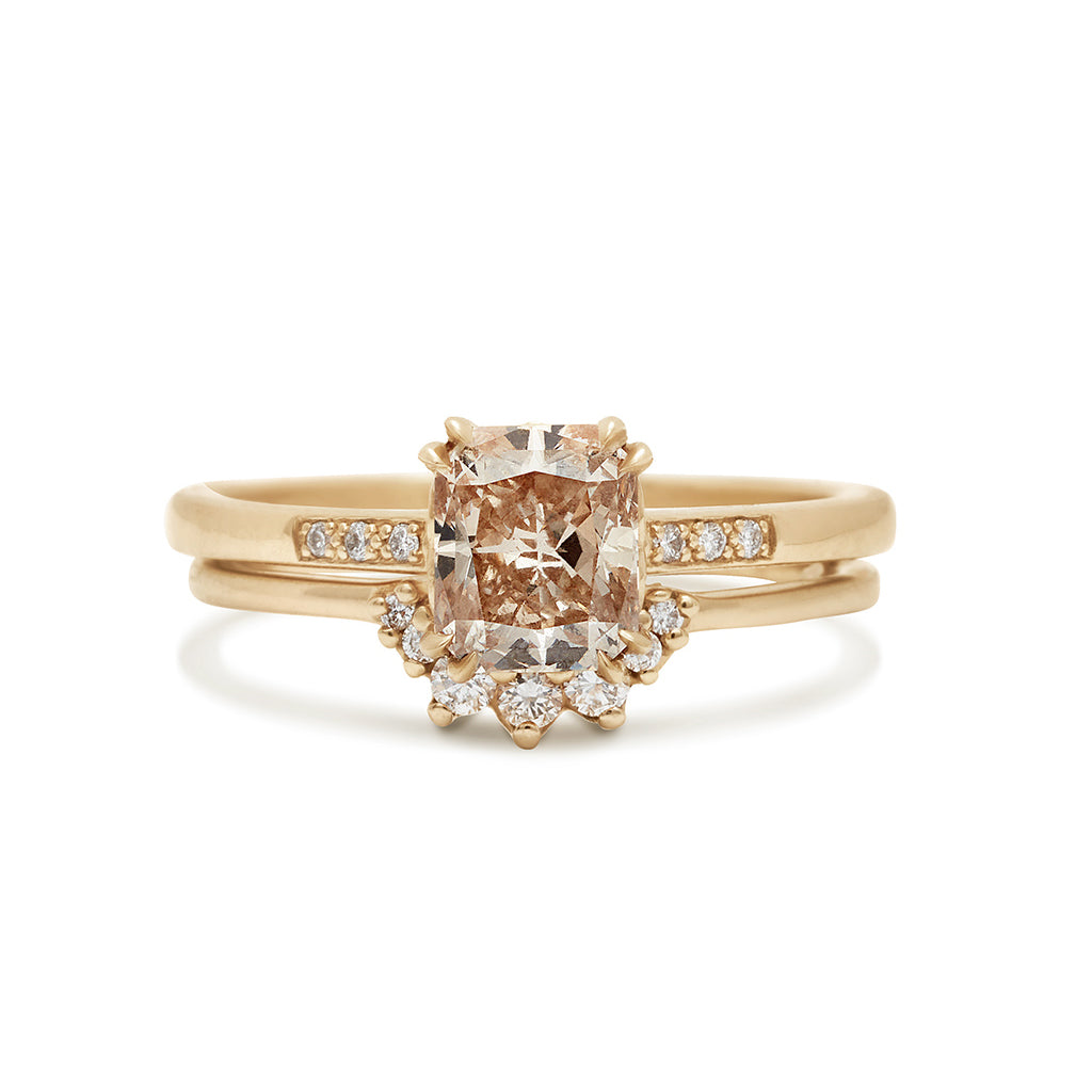 A solitaire ring with a 1.00ct cushion cut champagne diamond with white diamond pave on either side set in yellow gold above a 7 tiny white diamond curve band.