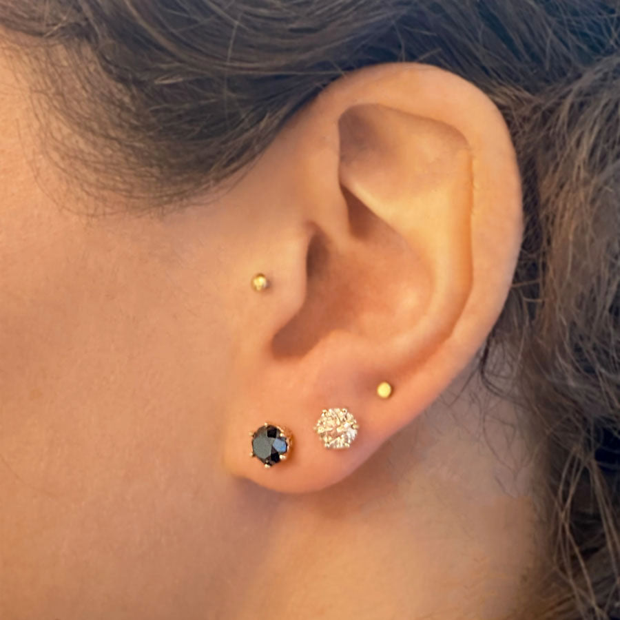 Two diamond stud earrings set in an intricate basket in yellow gold, one black diamond and one champagne diamond, on a medium-complexion model's ear.