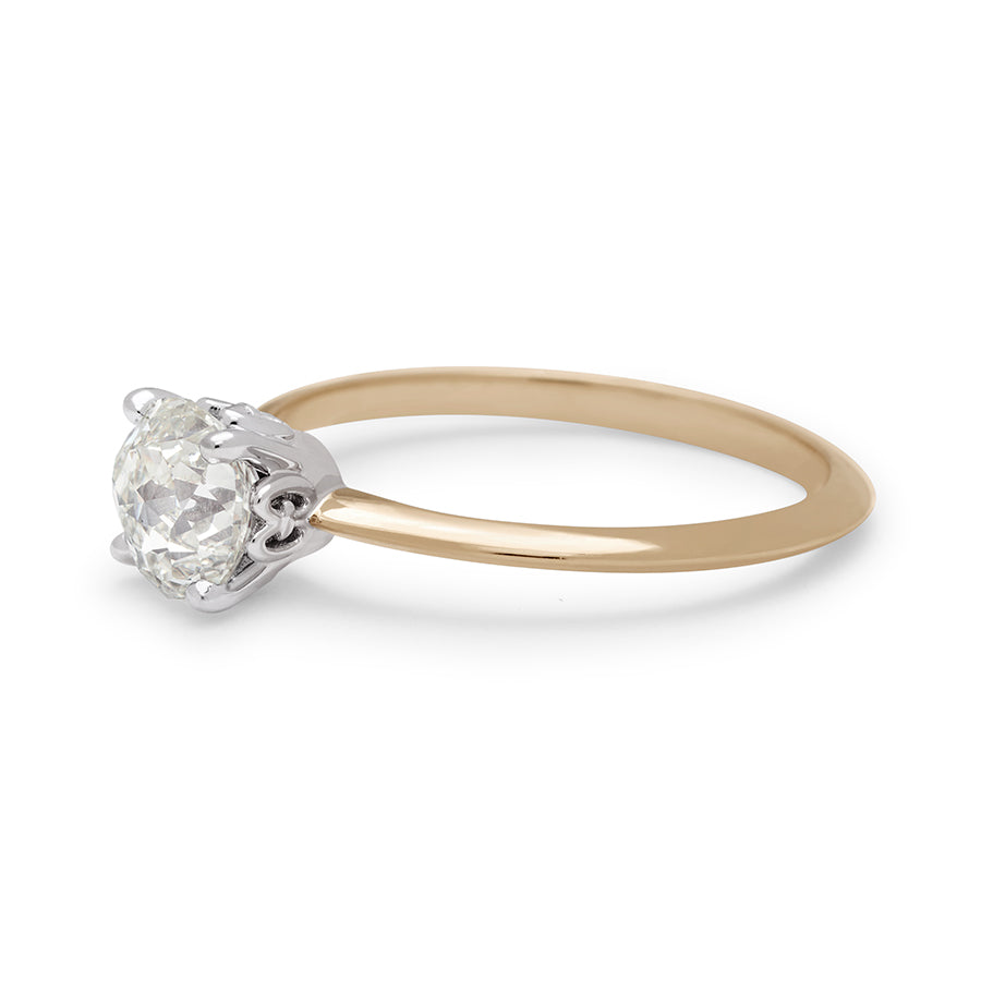 Angled view of a ring with a brilliant cut and round shape Crown Jubilee white diamond center stone in a white gold basket set in a knife edge yellow gold band.