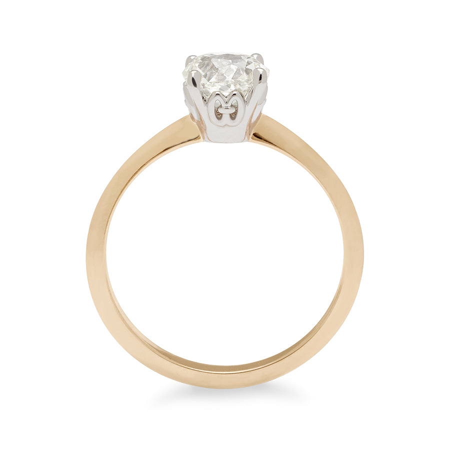 Side view of a ring with a brilliant cut and round shape Crown Jubilee white diamond center stone in a white gold basket set in a knife edge yellow gold band.