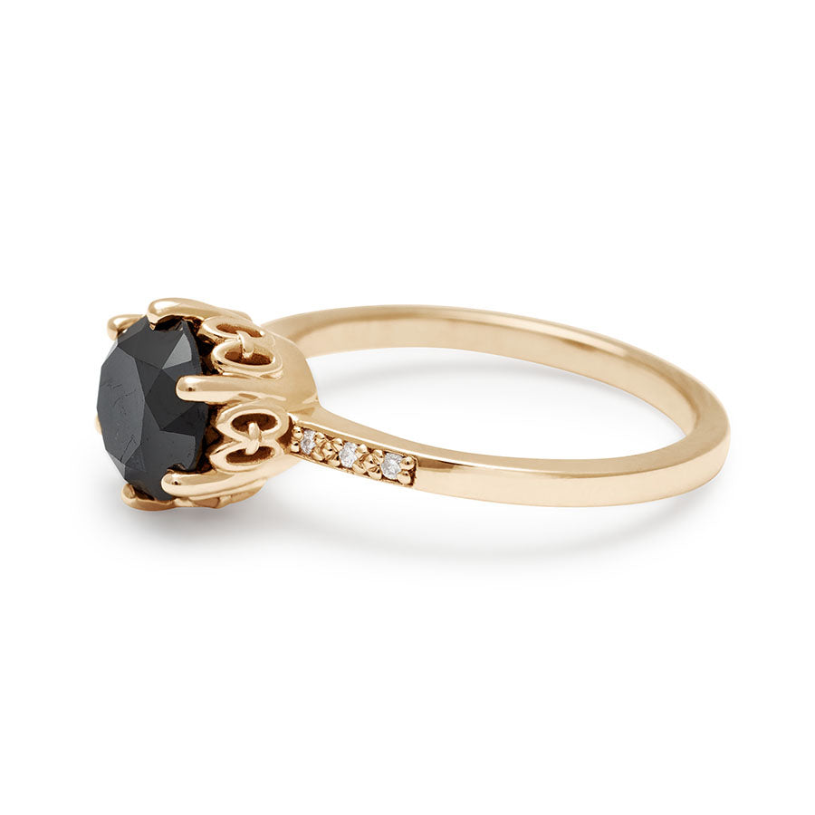 Angled view of solitaire ring with a round black diamond with white diamond pave on either side set in yellow gold.
