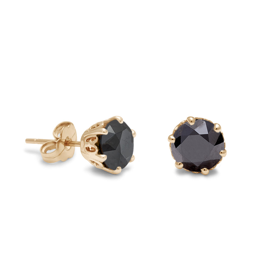 A pair of black diamond stud earrings set in an intricate basket in yellow gold one earring angled.