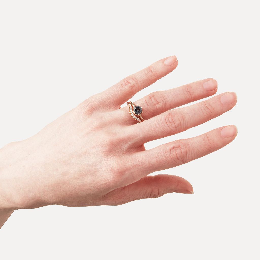 A solitaire ring with a round grey spinel with white diamond pave on either side set in yellow gold above an 11 white diamond curve band on a light-complextion ring finger on a pink background., White Gold, Rose Gold, Yellow Gold