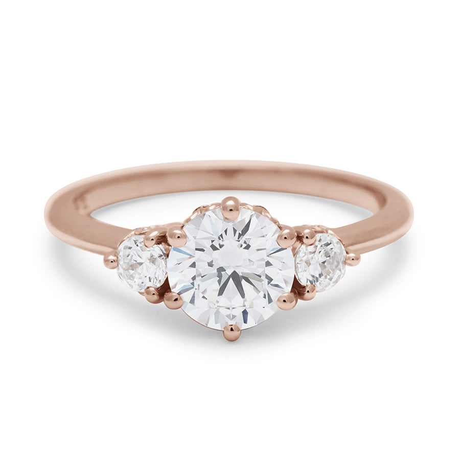 A three stone engagement ring with a round shape white diamond center stone with two white diamond round side stones set in rose gold., Rose Gold