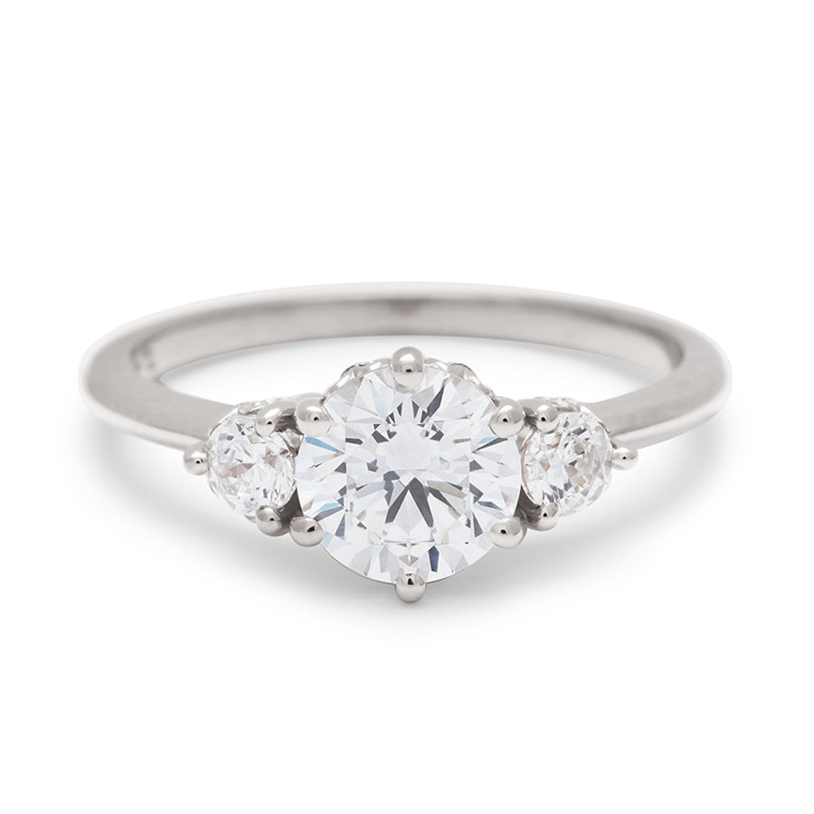 A three stone engagement ring with a round shape white diamond center stone with two white diamond round side stones set in white gold., White Gold