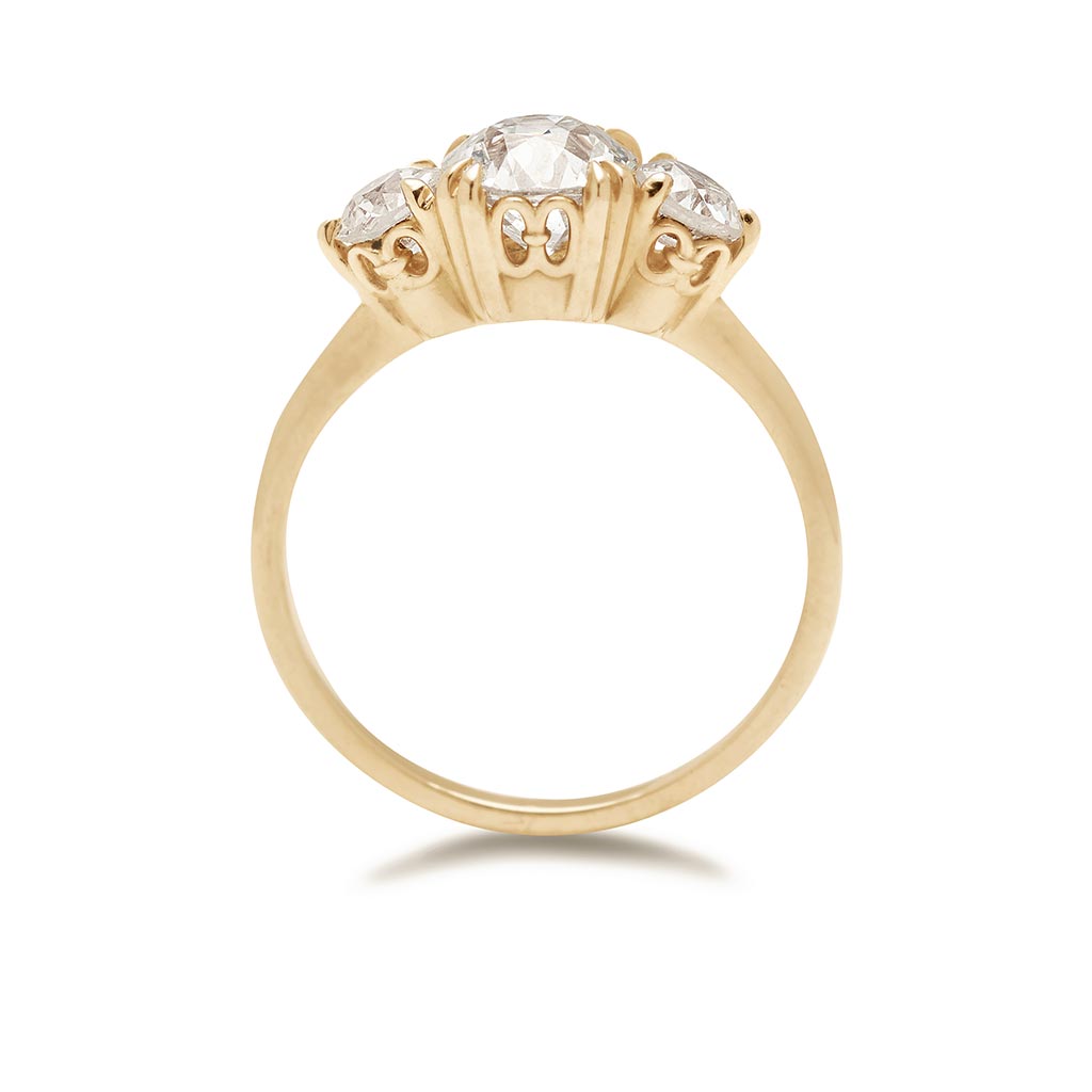 Side view of a three stone engagement ring with a round shape old mine cut white diamond center stone with two white diamond round side stones set in yellow gold.