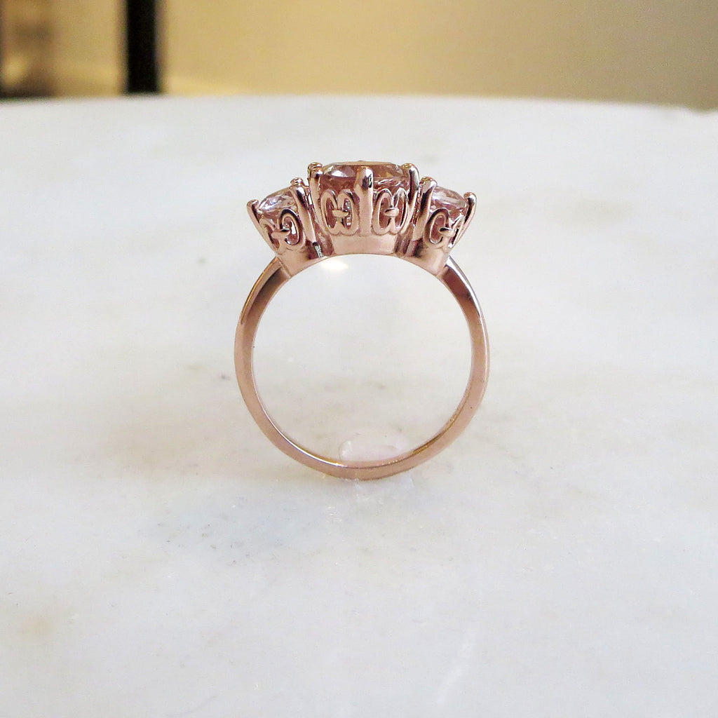 Side view of a three stone engagement ring with a round shape pink morganite center stone with two pink morganite round side stones set in rose gold.