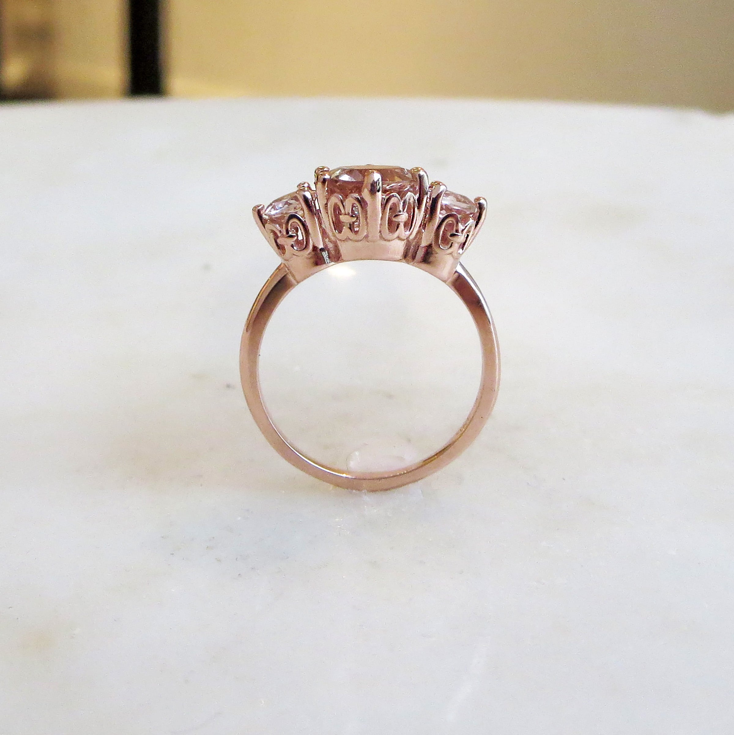 Side view of a three stone engagement ring with a round shape pink morganite center stone with two pink morganite round side stones set in rose gold.