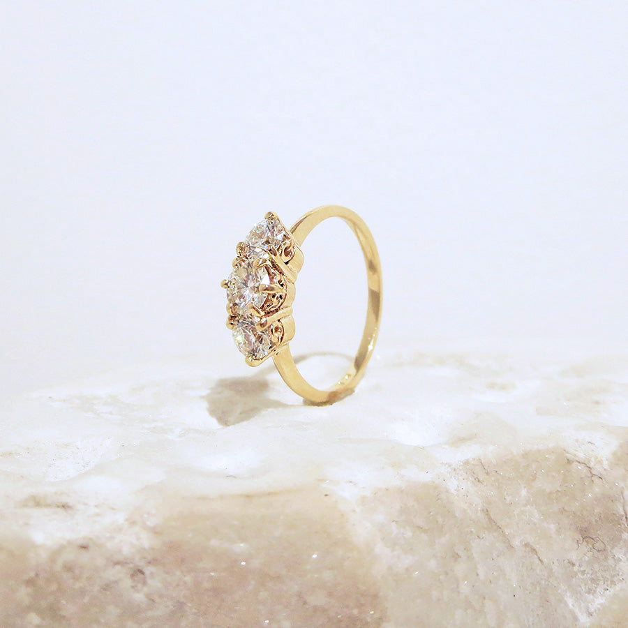 Angled view of a three stone engagement ring with a round shape champagne diamond center stone with two white diamond round side stones set in yellow gold on a white stone.