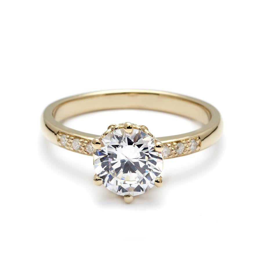 A solitaire ring with a round brilliant cut white diamond with white diamond pave on either side set in yellow gold., Yellow Gold