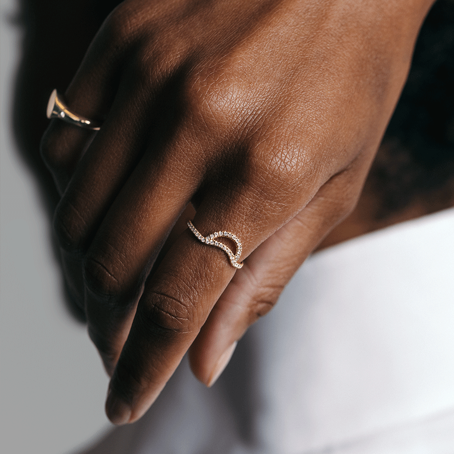 A helios band with white diamond pave set in yellow gold on a dark-complextion pointer finger and a signet ring on its pinky finger. Available in Rose Gold, Yellow Gold, White Gold.